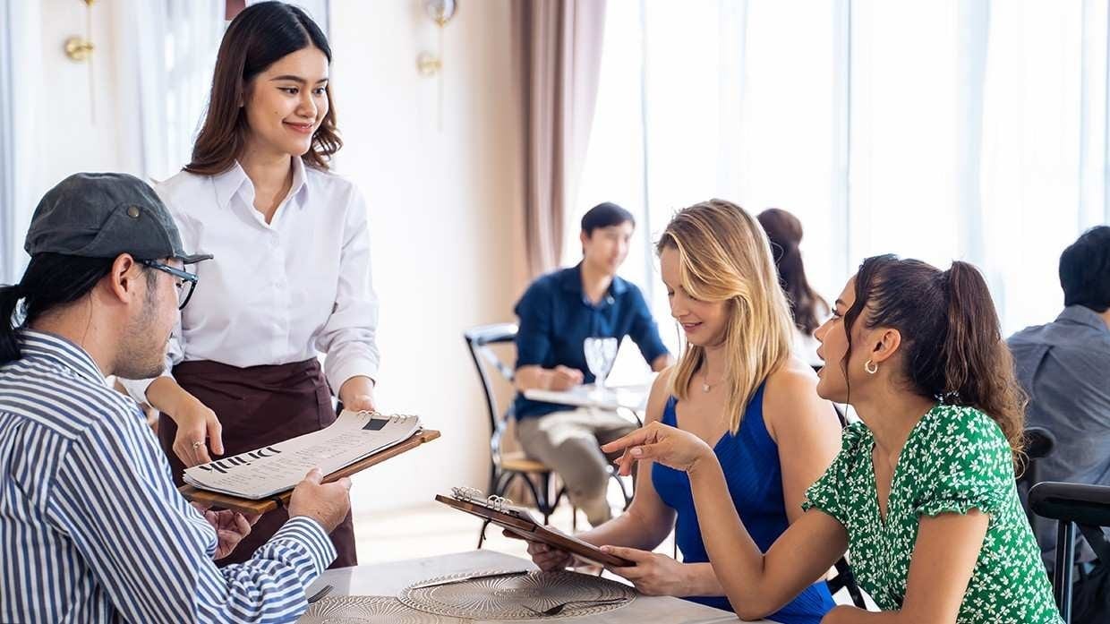 A female server presenting the menu to three diners at their table. A female server presenting the menu to three diners at their table.