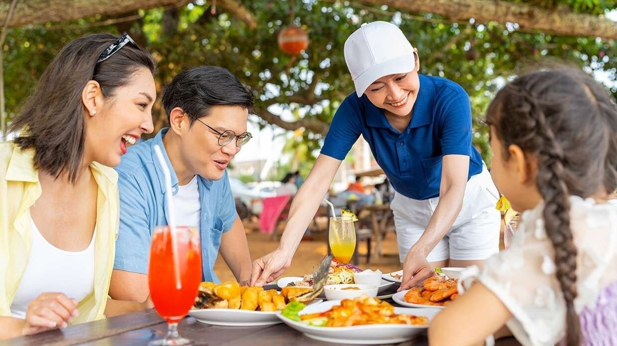 A waitress serving food to a family of three in an outdoor setting. A waitress serving food to a family of three in an outdoor setting.