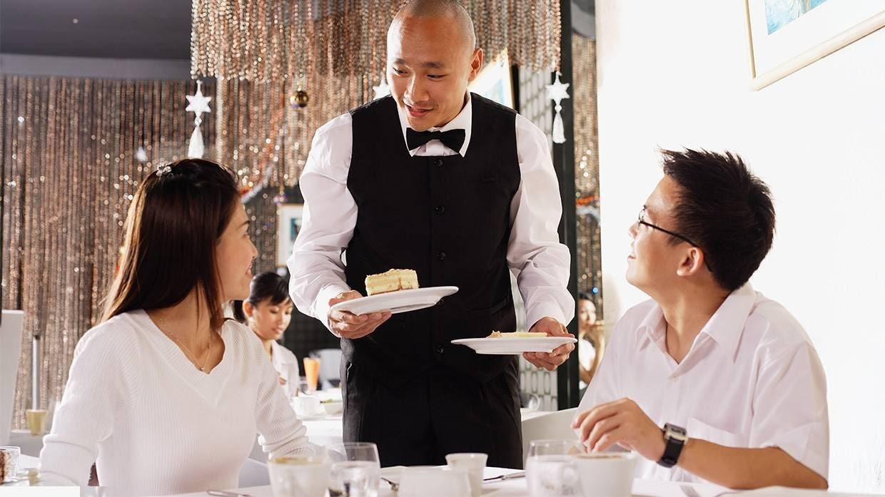 A waiter serving desserts to a couple. A waiter serving desserts to a couple.